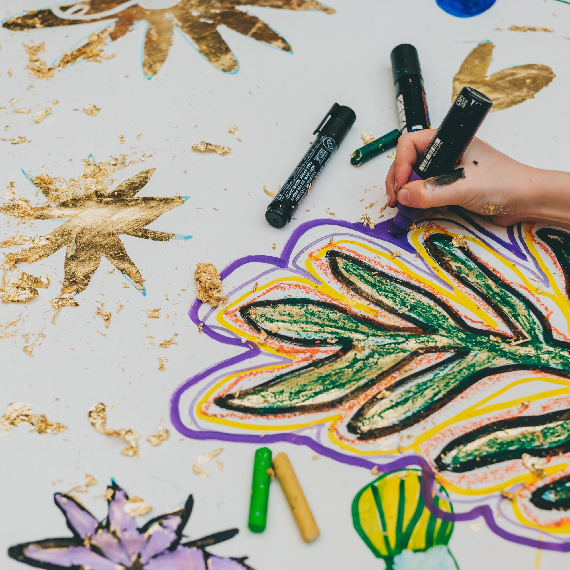 Cette photo représente un atelier pour enfants. L'enfant tient un feutre Posca et décore une fresque qui a été dorée à la feuille.