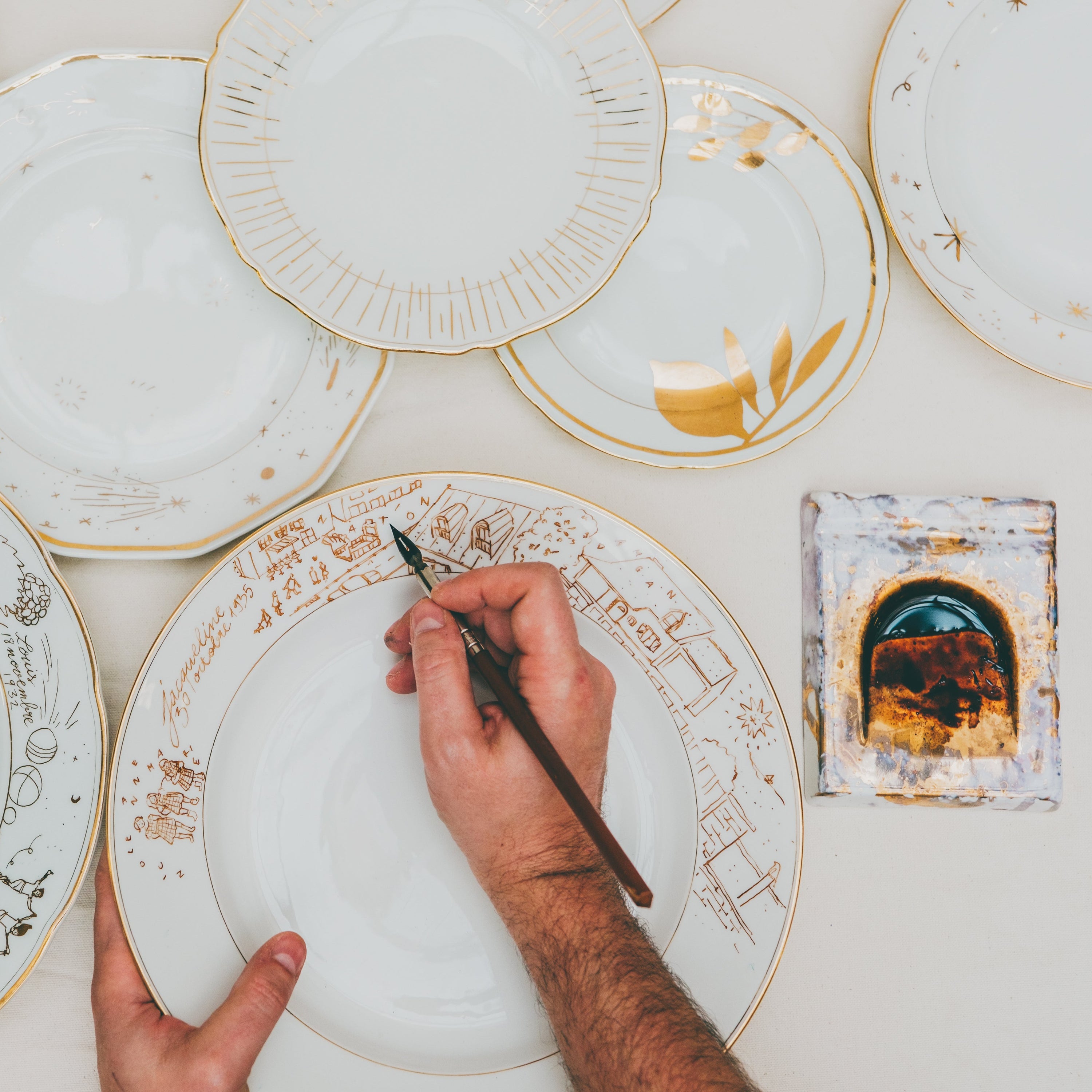 Cette photo représente un ensemble d'assiettes qui ont été décorées à l'or et à la plume lors d'un atelier de 3h à l'Atelier Grand Soleil à Paris