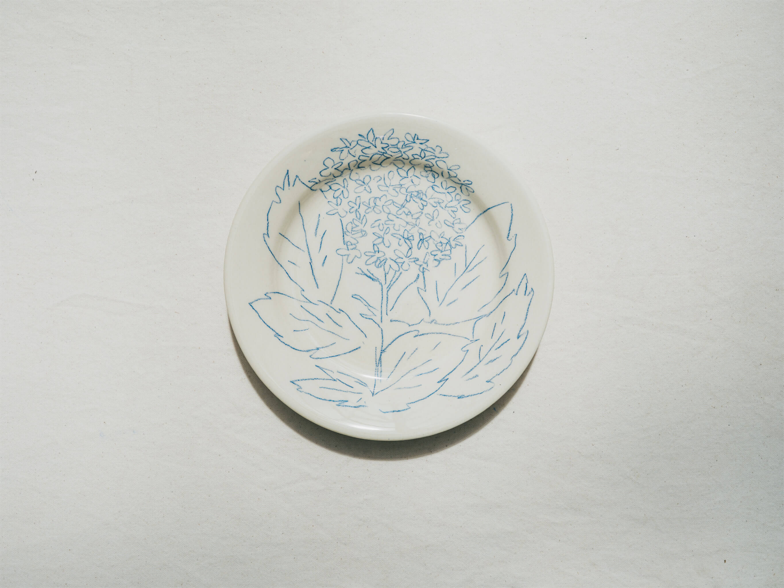 Assiette en faience décorée au crayon à oxydes puis émaillée par l'atelier grand soleil, à Paris. Personnalisable avec une phrase. Motif : hortensia
