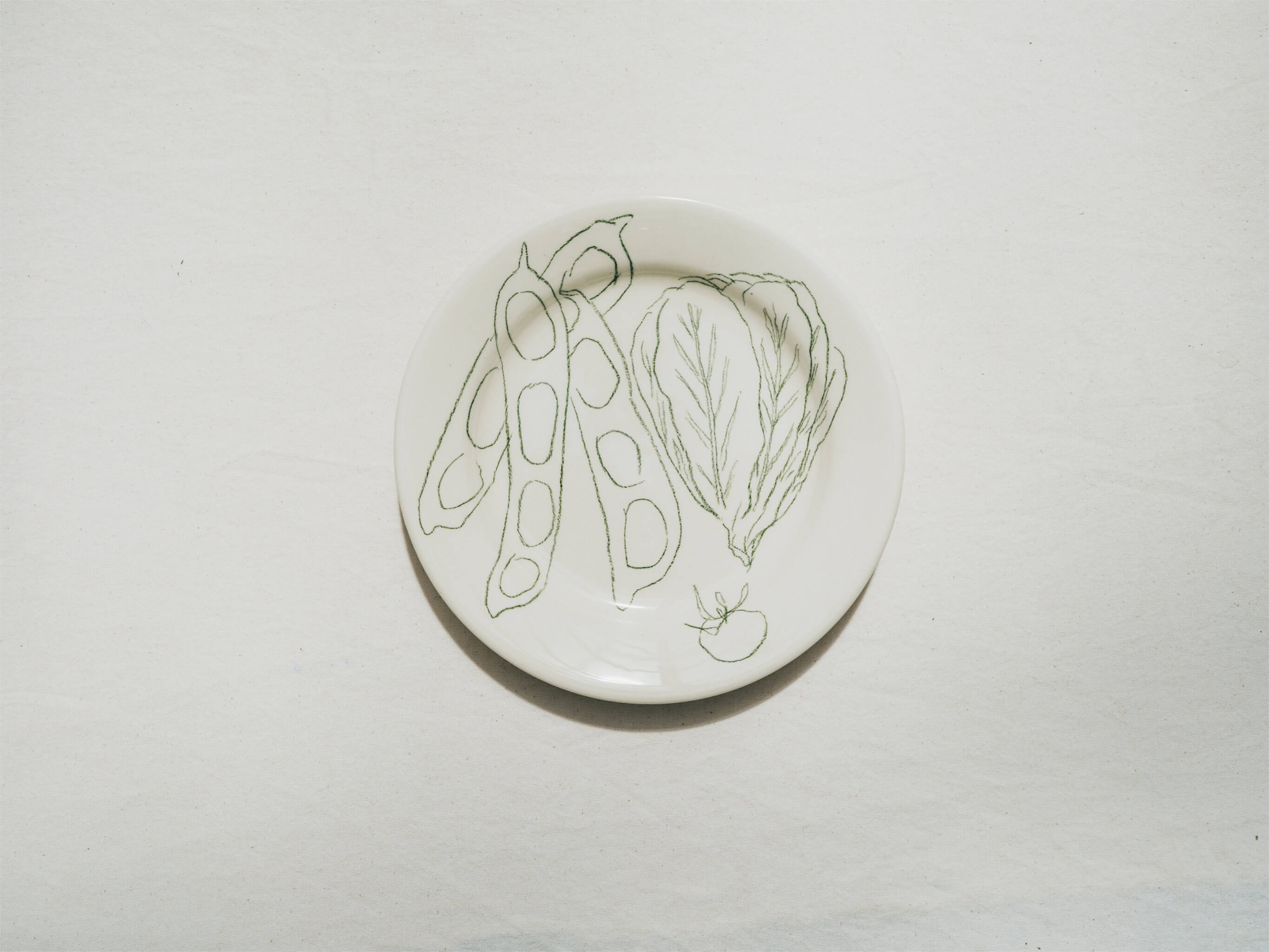 Assiette en faience décorée au crayon à oxydes puis émaillée par l'atelier grand soleil, à Paris. Personnalisable avec une phrase. Motif : fèves et sucrine