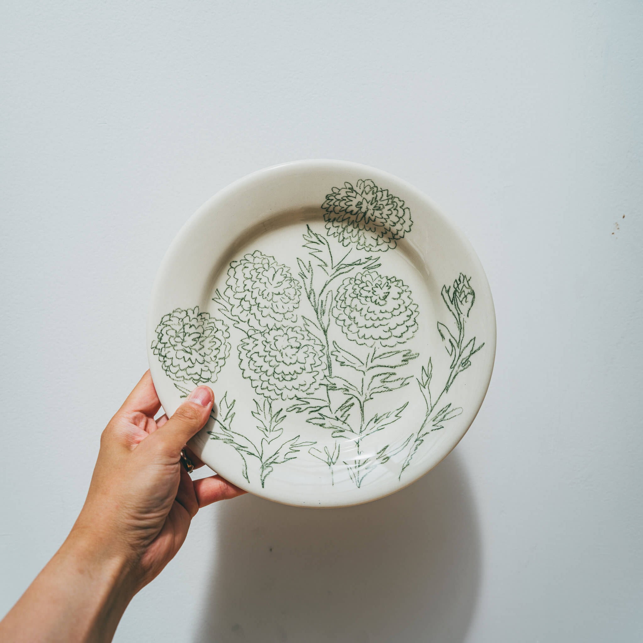 Assiette en faience décorée au crayon à oxydes puis émaillée par l'atelier grand soleil, à Paris. Personnalisable avec une phrase. Motif : dahlia