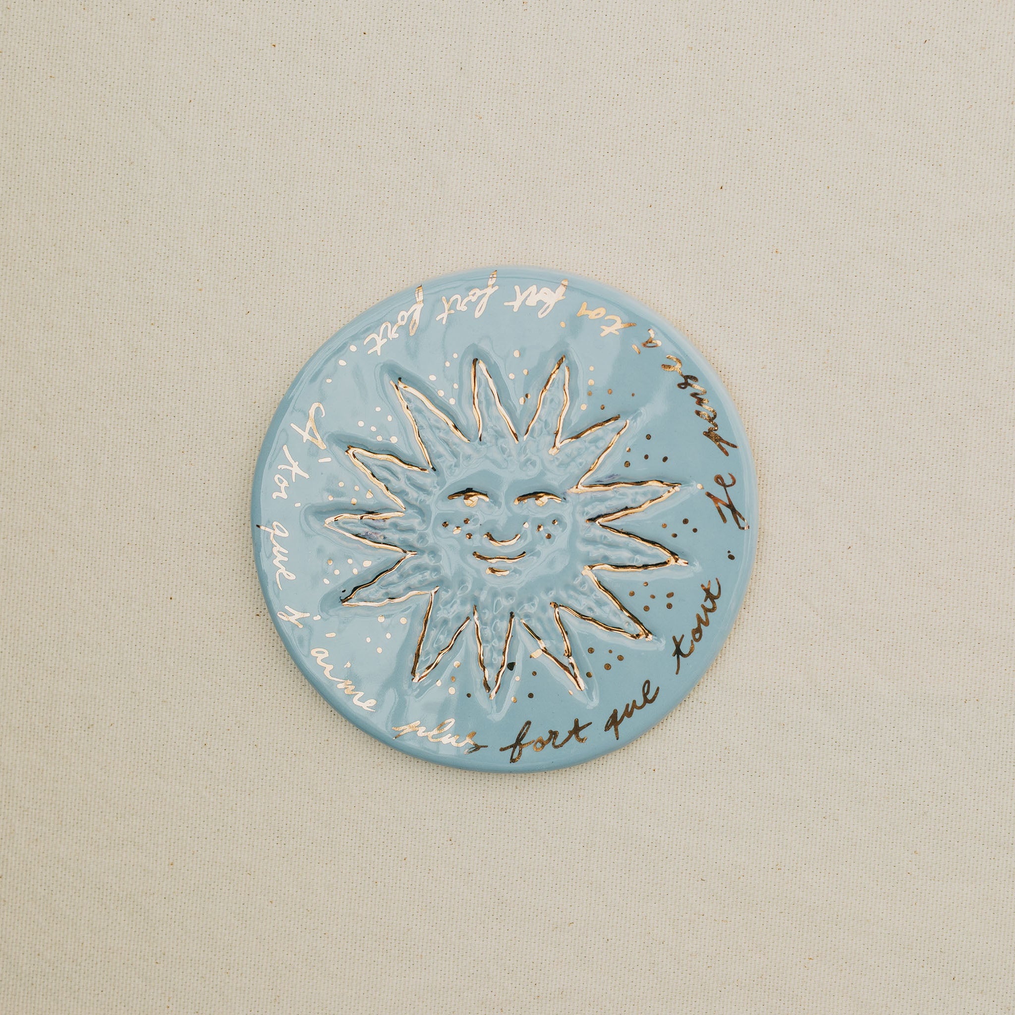 Médaille petit soleil en faïence personnalisée à la main, à l'or et à la plume. Atelier grand soleil. Couleur : bleu clair
