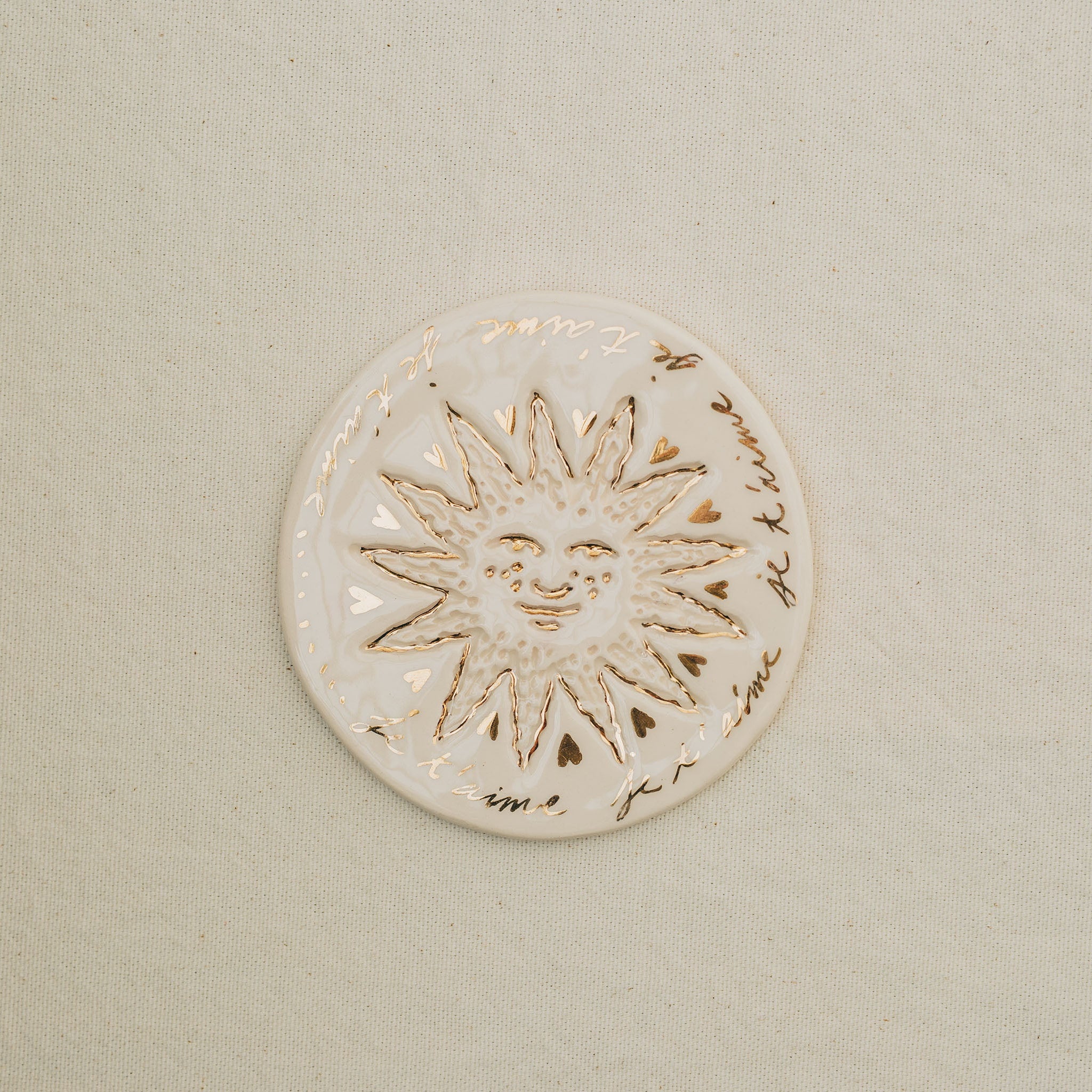 Médaille petit soleil en faïence personnalisée à la main, à l'or et à la plume. Atelier grand soleil. Couleur : blanc