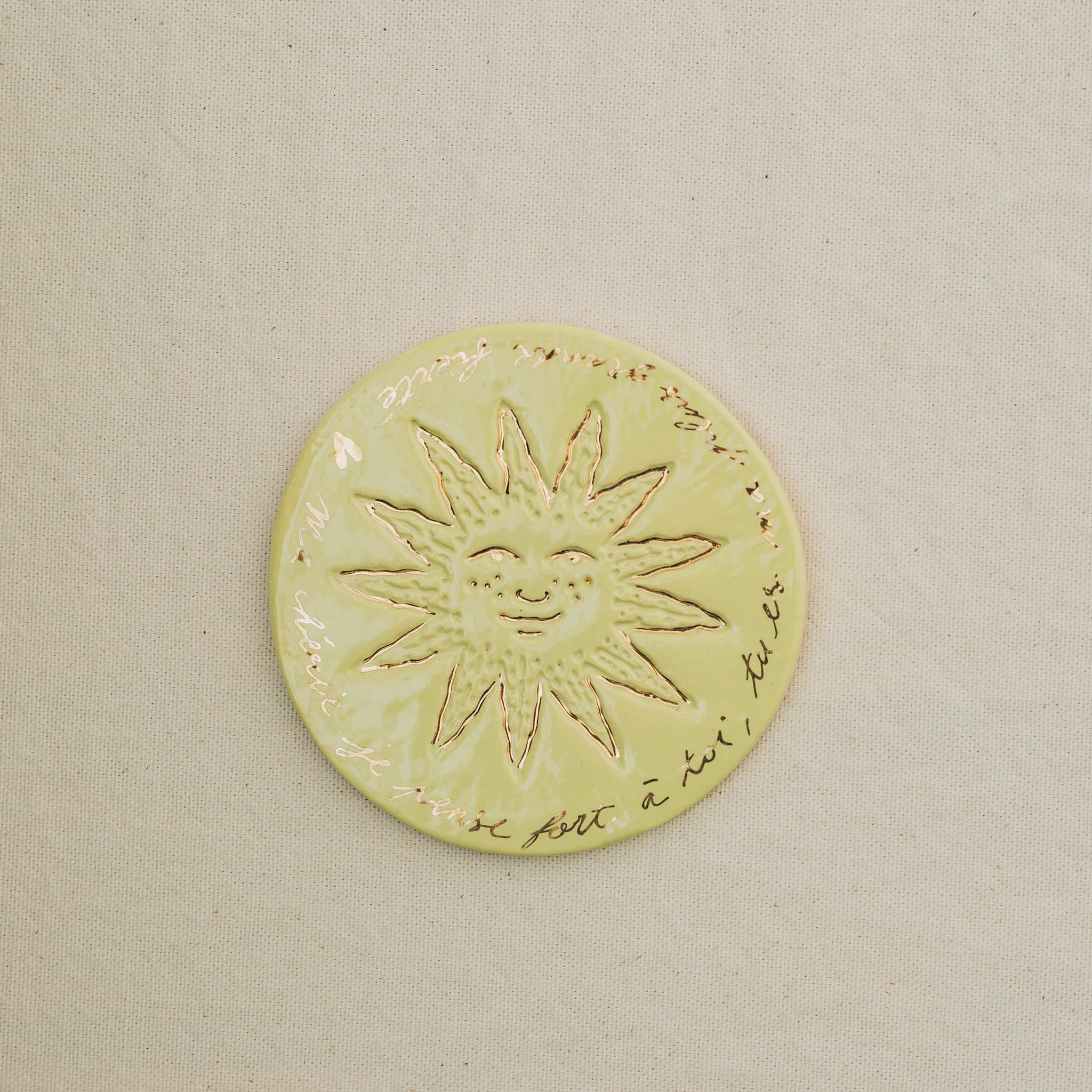 Médaille petit soleil en faïence personnalisée à la main, à l'or et à la plume. Atelier grand soleil. Couleur : anis