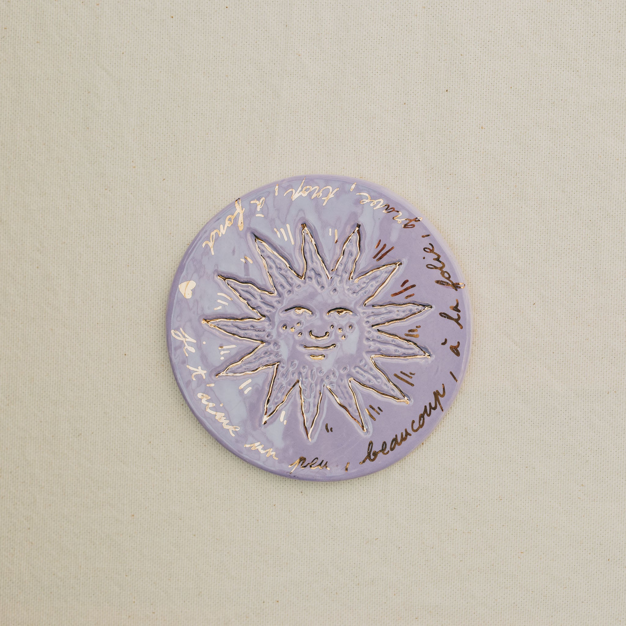 Médaille petit soleil en faïence personnalisée à la main, à l'or et à la plume. Atelier grand soleil. Couleur : mauve
