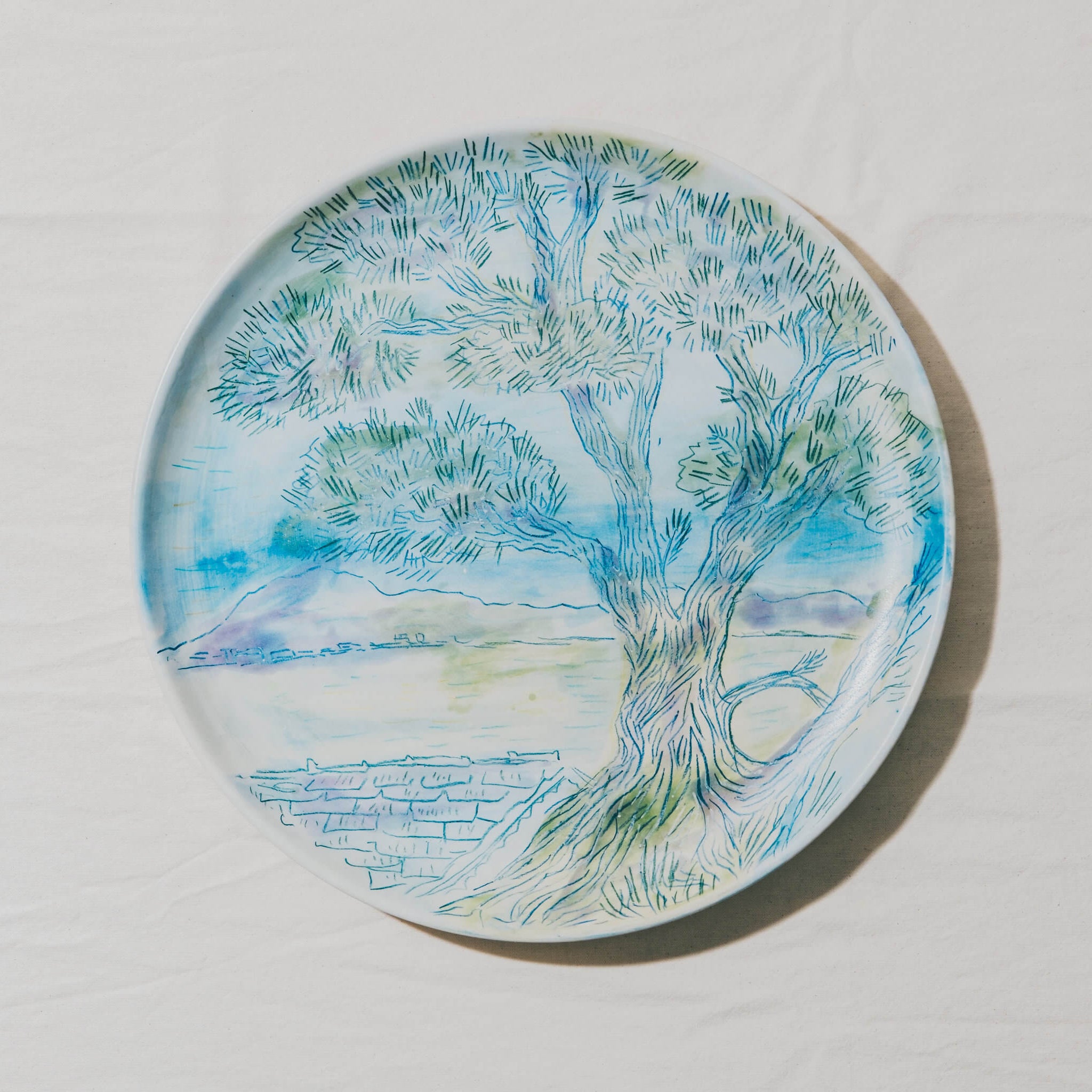 Plat moulé à l’Atelier Grand Soleil, en faïence décorée au crayon à oxyde, à l’engobe puis émaillée transparent.
Les plats sont compatibles avec un lavage en machine en mode éco.
Possibilité de personnalisation à l'or et à la plume. 
Motif : paysage d'arbres, dans les tons bleus et verts
