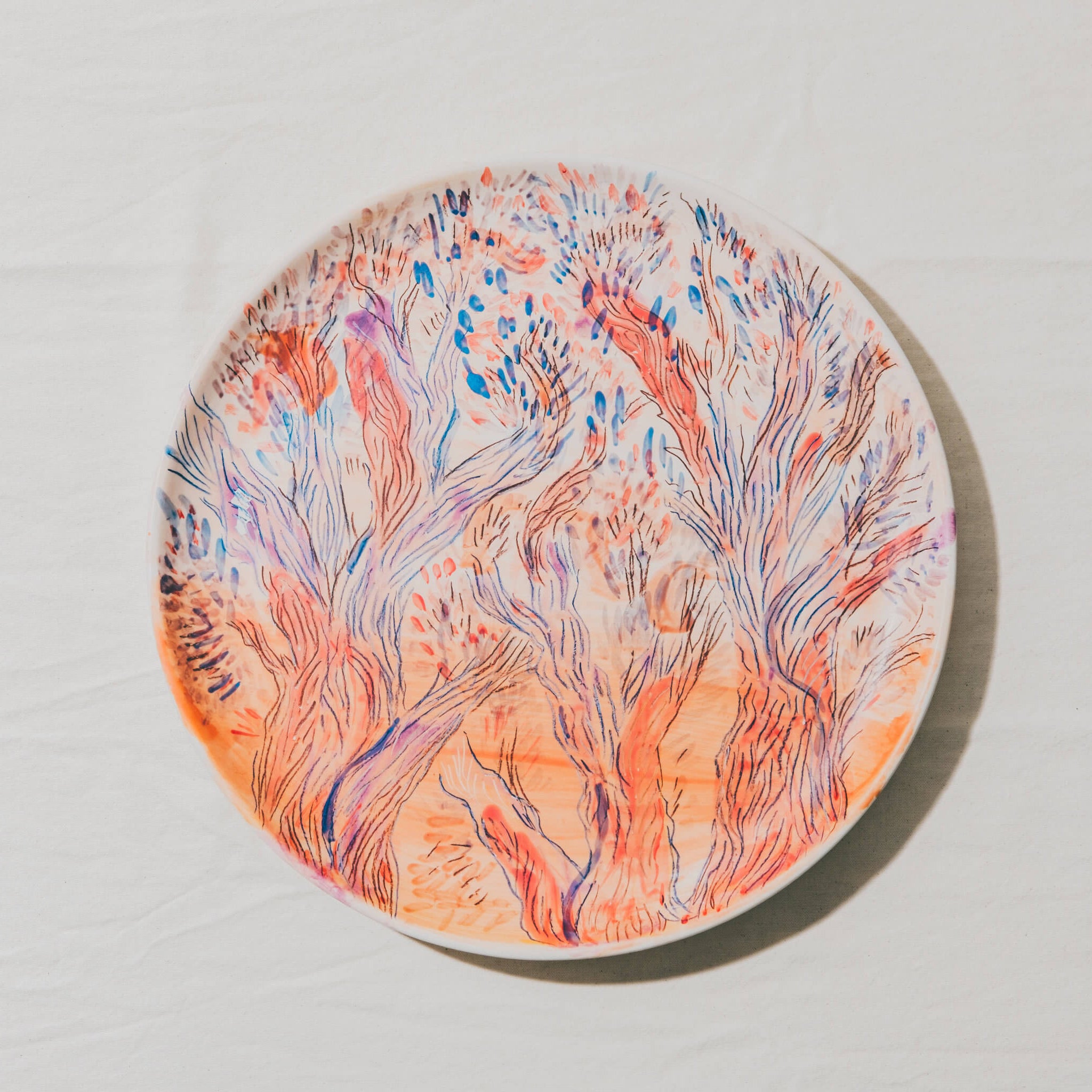 Plat moulé à l’Atelier Grand Soleil, en faïence décorée au crayon à oxyde, à l’engobe puis émaillée transparent.
Les plats sont compatibles avec un lavage en machine en mode éco.
Possibilité de personnalisation à l'or et à la plume. 
Motif : paysage d'arbres, dans les tons orange et rouge avec des touches de bleu
