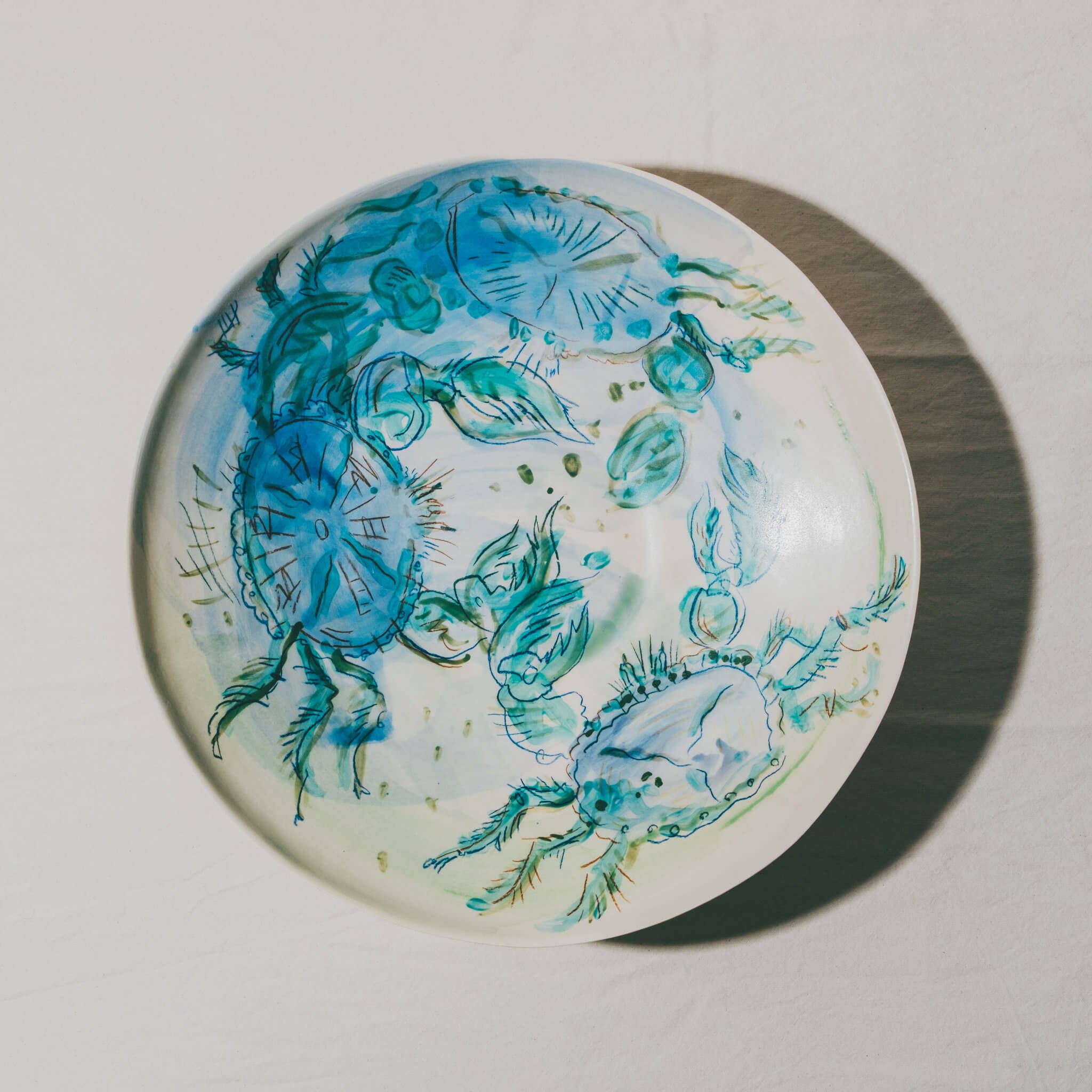Plat coupe moulé à l’Atelier Grand Soleil, en faïence décorée au crayon à oxyde, à l’engobe puis émaillée transparent.
Les plats sont compatibles avec un lavage en machine en mode éco.
Possibilité de personnalisation à l'or et à la plume. 
Motif : crabes, dans les tons vert et bleu