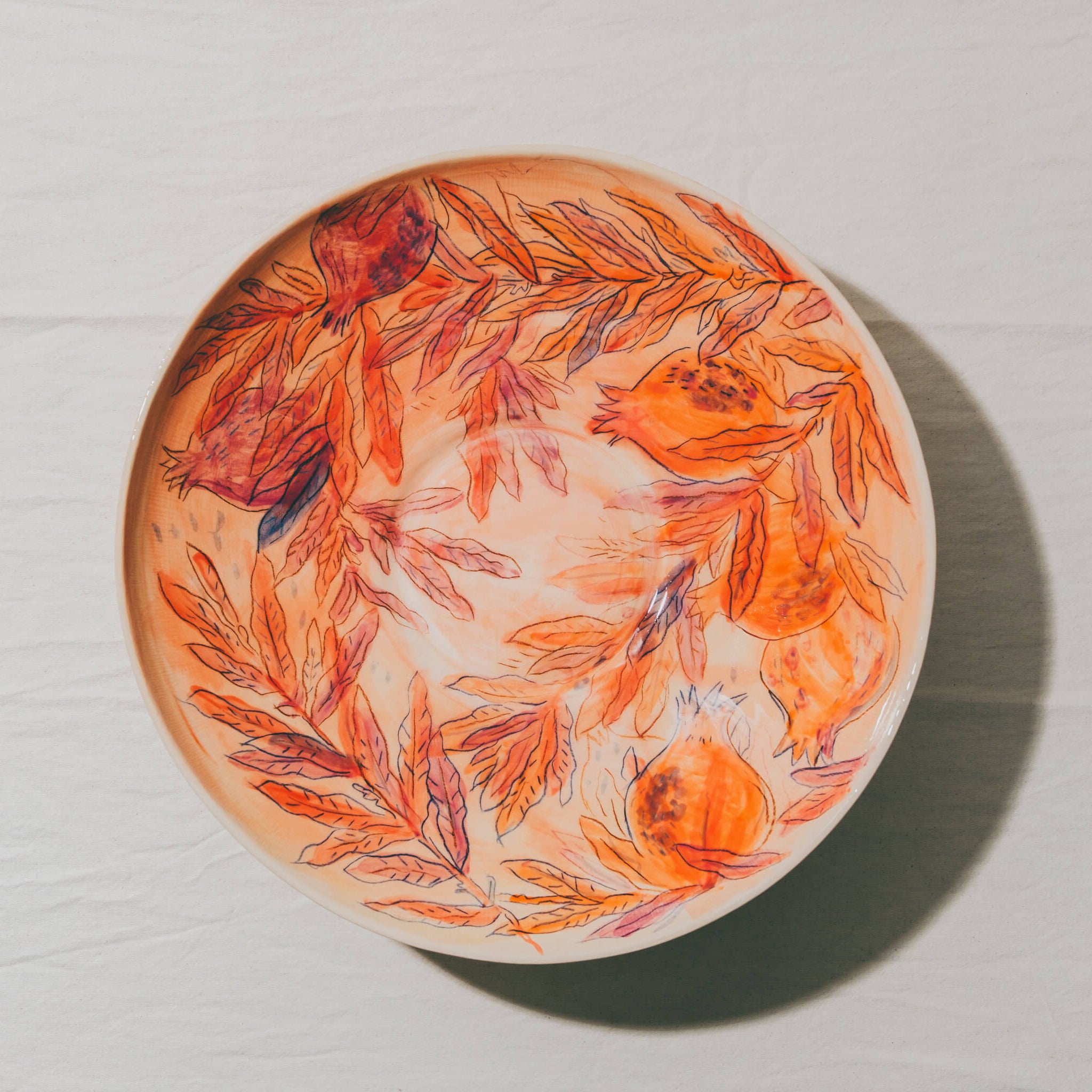 Plat coupe moulé à l’Atelier Grand Soleil, en faïence décorée au crayon à oxyde, à l’engobe puis émaillée transparent.
Les plats sont compatibles avec un lavage en machine en mode éco.
Possibilité de personnalisation à l'or et à la plume. 
Motif : grenades et feuilles, dans les tons orange et rouge